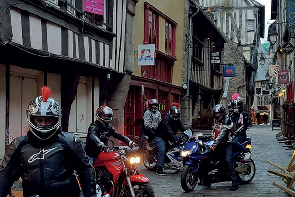 Une bonne adresse pour vous qui partez en balade moto dans le secteur de Dinan : le Gex Bar ! Situé rue de la Cordonnerie, plus connue comme étant la rue de la Soif, le Gex Bar est bien entendu tenu par un fan de moto, et vous l’aurez deviné, du modèle emblématique de chez Suzuki : le GSXR, jusqu’à se teindre les cheveux en bleu à l’occasion des 24h du Mans (une sombre histoire de pari perdu...) et de s’en faire tatouer un dans le dos ! Je vous rassure, quelle que soit votre marque fétiche, vous serez accueilli de la même manière et la déco du bar ne laisse rien paraître de cette passion débordante, y compris pendant la diffusion du MotoGP ou du SuperBike. Car oui, en toute logique, le Gex Bar vous propose la diffusion des courses et modifie même ses horaires d’ouverture en fonction de celles-ci ! Vous pouvez ainsi vous y arrêter pour regarder votre discipline préférée dans une des deux salles à votre disposition. Et si vous prévenez de votre venue, Benoît peut prévoir de quoi vous restaurer. Le Gex Bar est le lieu de rendez-vous de groupes comme le "GSXR de Bretagne" ou encore le "BZH Pony Trekking 22/35", c'est aussi le point de départ ou d'arrivée de balades motos, parfois organisées par Benoît lui-même pour les 24h du Mans, le GP de France ou encore à l'occasion de Porcaro ! Dans ces cas-là, le bar est fermé et les courses enregistrées pour être rediffusées les jours suivants. Si vous souhaitez vous attarder après les courses, vous pourrez déguster un des nombreux rhums que Benoît vous propose. Et on touche là à la seconde passion de notre hôte, les rhums et notamment les rhums arrangés faits maison bien entendu et à consommer avec modération. Notez que le Gex Bar est ouvert tous les jours, sauf le lundi, de 17h à 2h de mai à septembre et de 17h à 1h en période hivernal, et bien sûr aux heures des courses diffusées !